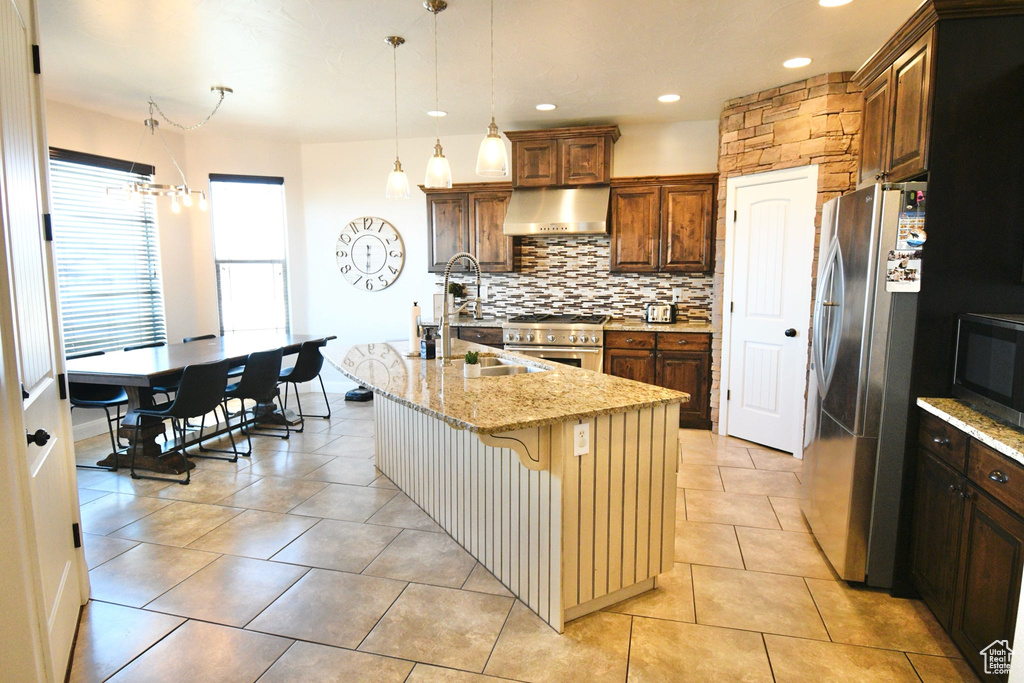 Kitchen with backsplash, a center island with sink, stainless steel appliances, wall chimney range hood, and a kitchen breakfast bar
