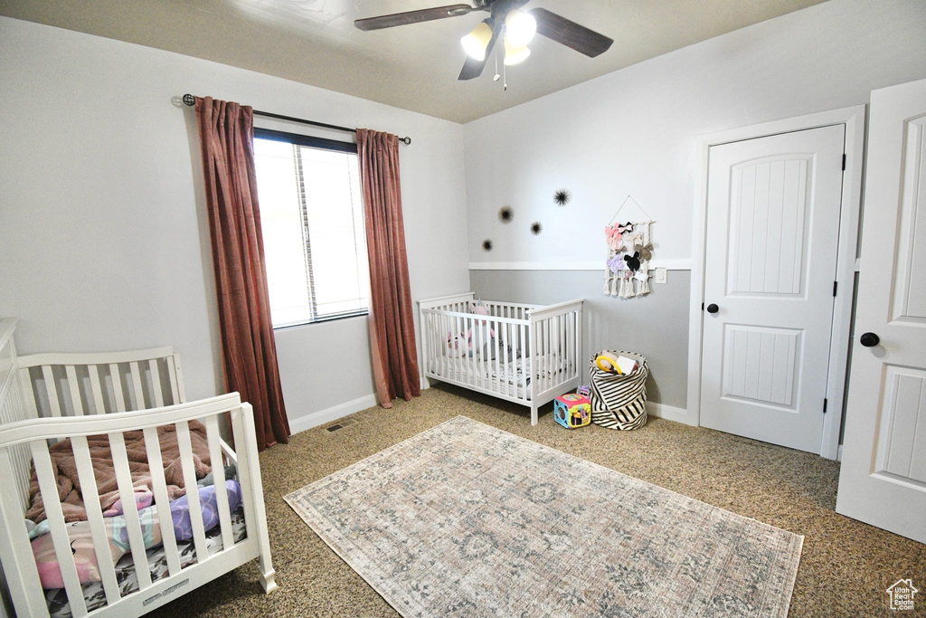 Bedroom with ceiling fan, a crib, and carpet flooring
