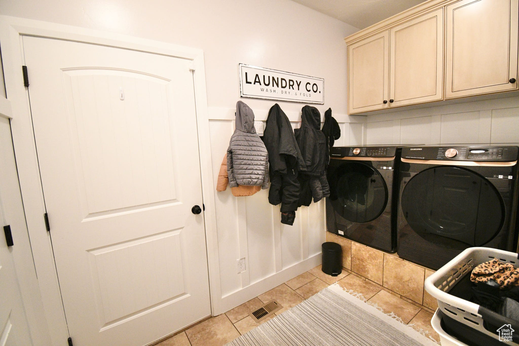 Clothes washing area with cabinets, light tile floors, and separate washer and dryer
