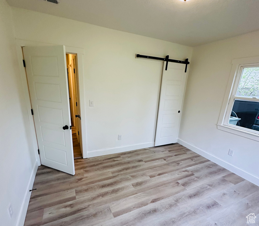 Unfurnished bedroom featuring wood-type flooring and a barn door