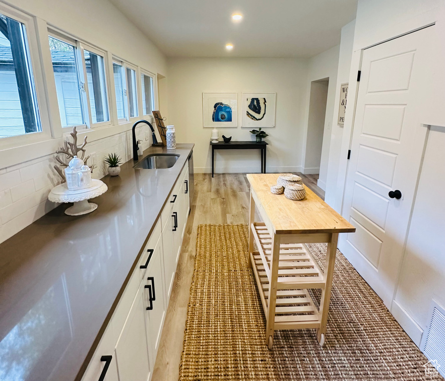 Kitchen with tasteful backsplash, light hardwood / wood-style flooring, white cabinets, and sink