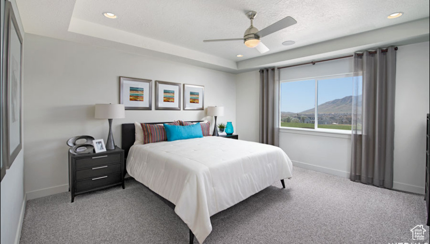 Carpeted bedroom with a mountain view, a textured ceiling, ceiling fan, and a tray ceiling