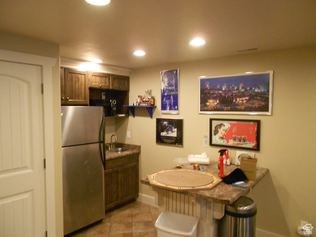 Kitchen featuring kitchen peninsula, sink, light tile floors, dark stone countertops, and stainless steel fridge