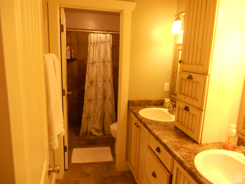 Bathroom featuring toilet, vanity with extensive cabinet space, double sink, and tile flooring