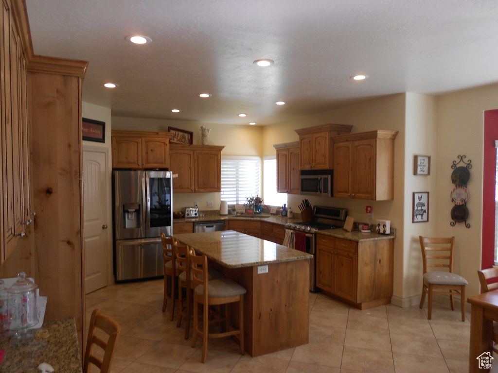 Kitchen featuring a kitchen island, stainless steel appliances, light tile floors, and a kitchen bar