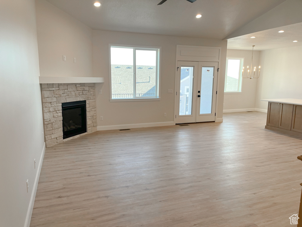 Unfurnished living room featuring light hardwood / wood-style floors, ceiling fan with notable chandelier, french doors, and a fireplace