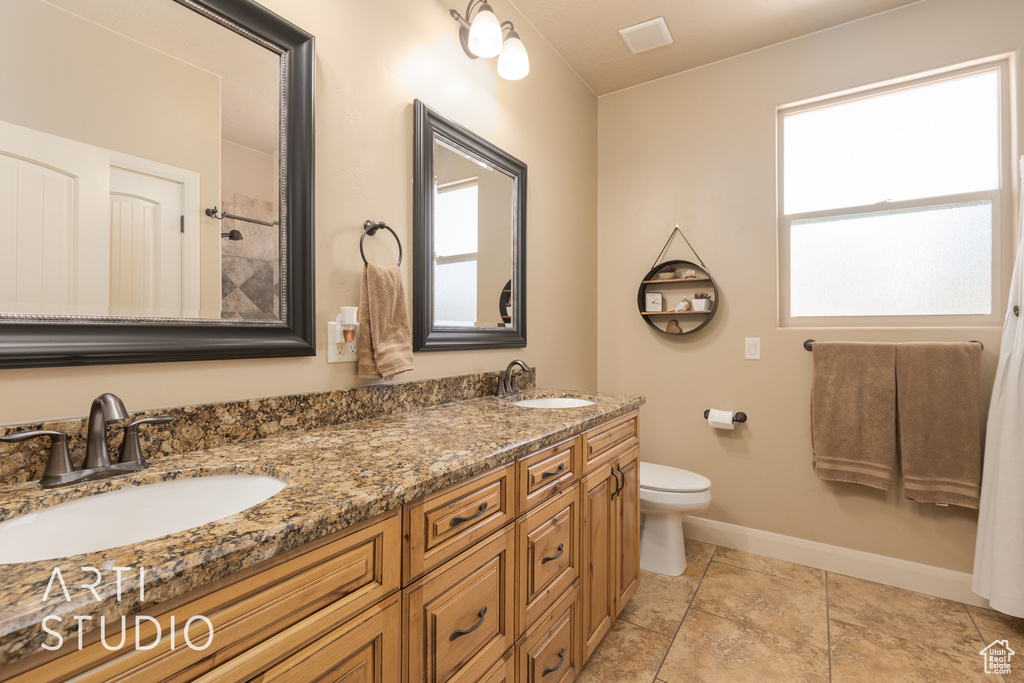 Bathroom featuring plenty of natural light, double vanity, tile floors, and toilet