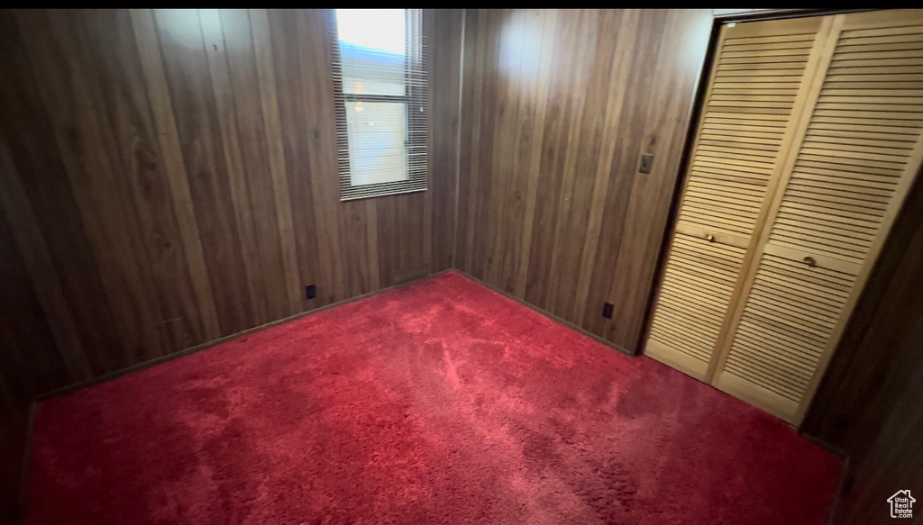 Unfurnished bedroom featuring a closet, wooden walls, and carpet flooring