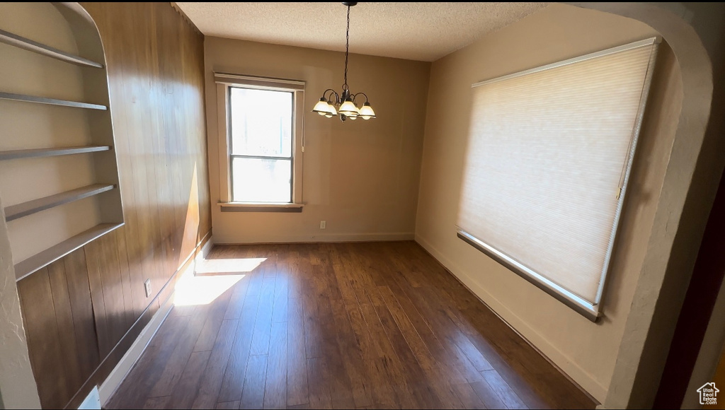 Unfurnished room featuring a textured ceiling, dark hardwood / wood-style flooring, and a chandelier