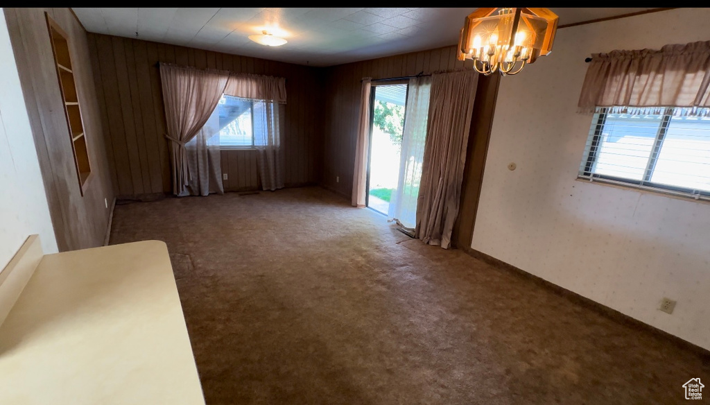 Spare room featuring carpet flooring, wood walls, and a notable chandelier
