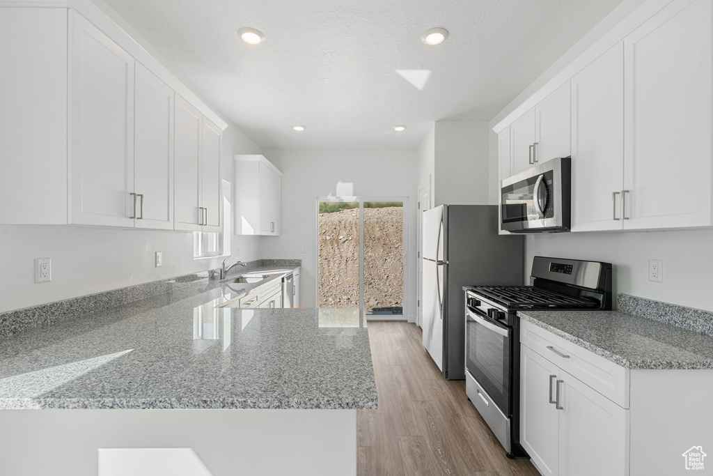 Kitchen with light stone countertops, appliances with stainless steel finishes, light hardwood / wood-style flooring, white cabinetry, and sink