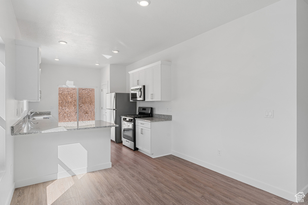 Kitchen featuring white cabinets, light stone countertops, hardwood / wood-style floors, appliances with stainless steel finishes, and sink