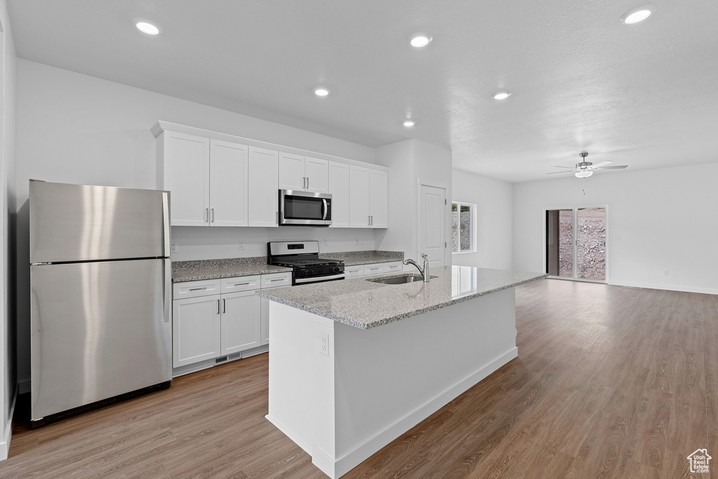 Kitchen with appliances with stainless steel finishes, ceiling fan, light hardwood / wood-style floors, white cabinetry, and sink