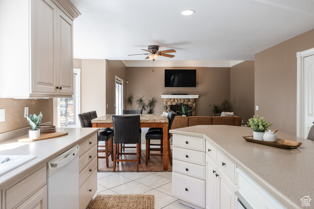 Kitchen featuring a stone fireplace, ceiling fan, dishwasher, white cabinets, and light tile floors