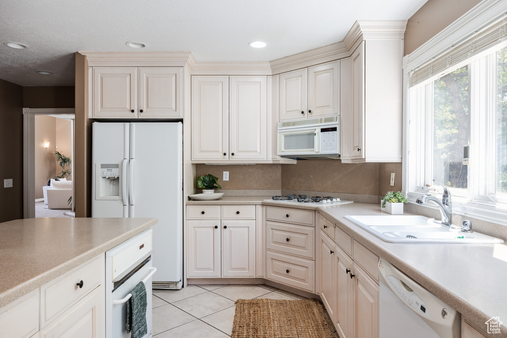 Kitchen featuring sink, white appliances, and light tile floors