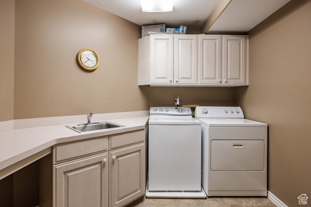 Washroom featuring cabinets, light tile floors, a textured ceiling, washing machine and clothes dryer, and sink