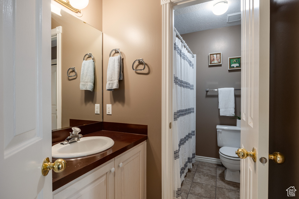 Bathroom with a textured ceiling, vanity, tile floors, and toilet