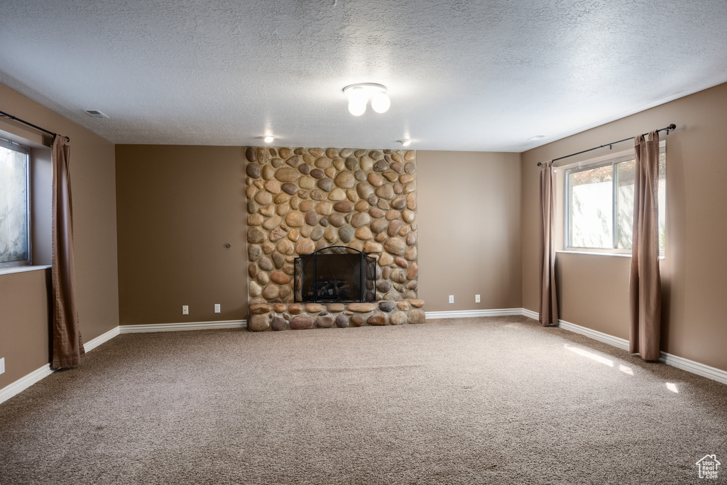 Unfurnished living room featuring a fireplace, a textured ceiling, and carpet flooring