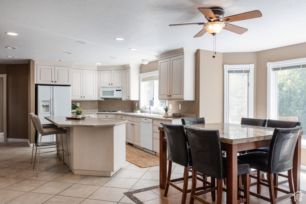 Kitchen featuring backsplash, white appliances, a center island, and light tile floors