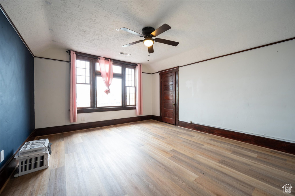 Empty room with hardwood / wood-style floors, vaulted ceiling, ceiling fan, and a textured ceiling