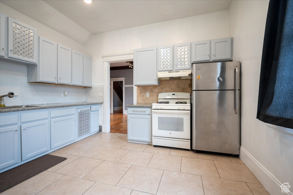 Kitchen with light tile flooring, stainless steel refrigerator, white range, sink, and tasteful backsplash