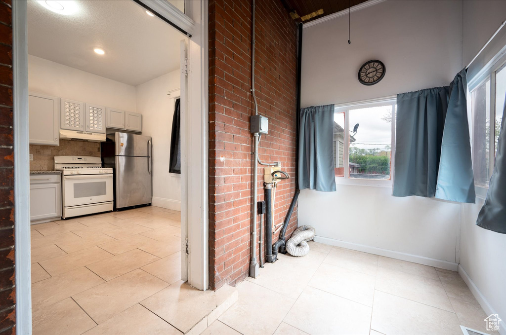 Kitchen featuring white range, backsplash, brick wall, stainless steel refrigerator, and light tile floors