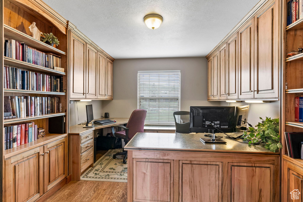 Office area featuring a textured ceiling, built in desk, and light hardwood / wood-style floors
