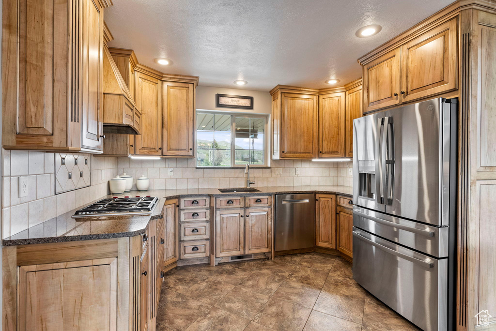Kitchen with stainless steel appliances, tile flooring, tasteful backsplash, dark stone countertops, and sink