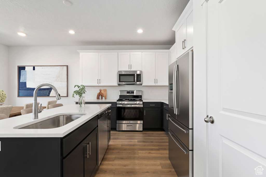 Kitchen with dark hardwood / wood-style flooring, white cabinetry, appliances with stainless steel finishes, sink, and an island with sink