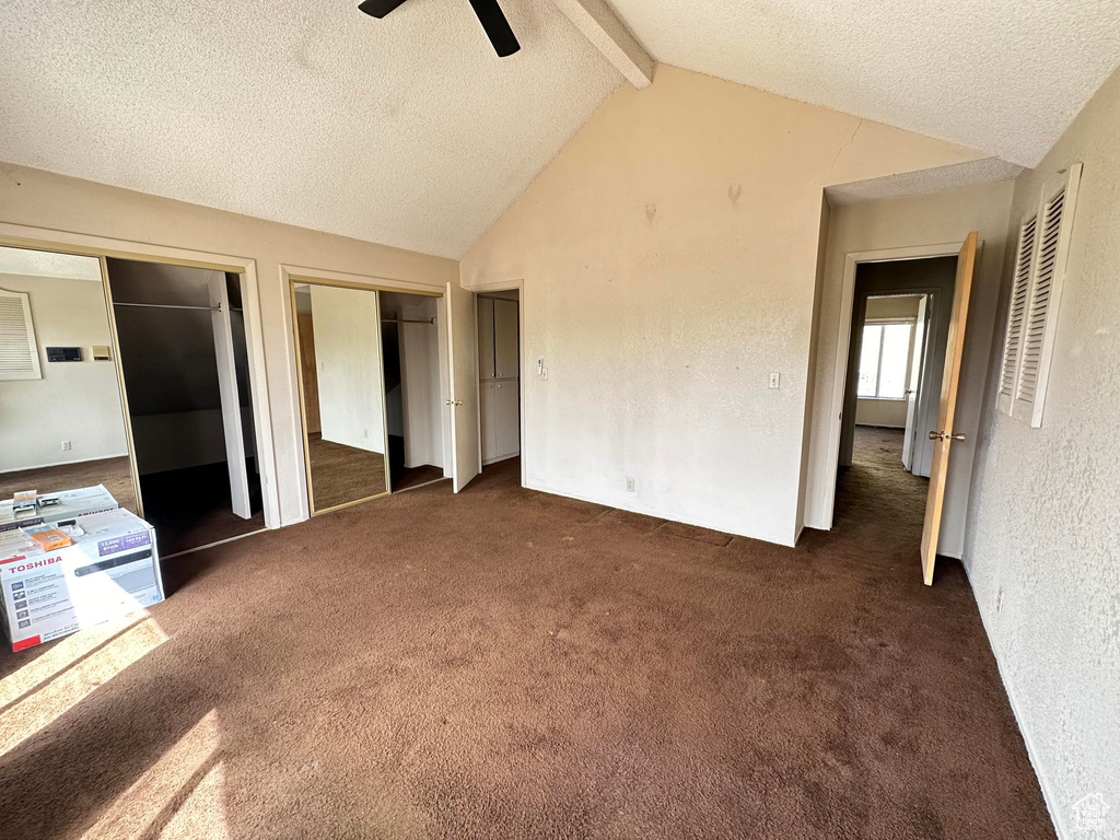 Unfurnished bedroom with lofted ceiling with beams, ceiling fan, dark carpet, and two closets
