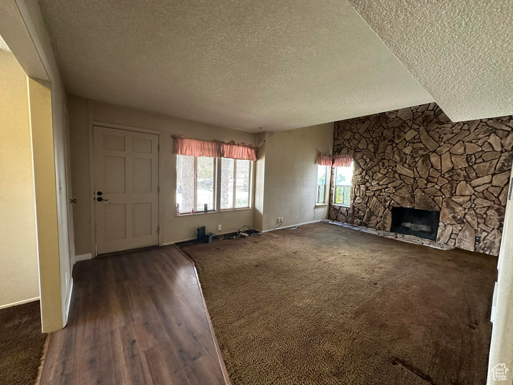 Unfurnished living room featuring a textured ceiling, a stone fireplace, and dark wood-type flooring