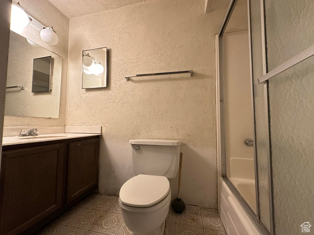 Full bathroom with vanity, toilet, tile floors, and bath / shower combo with glass door