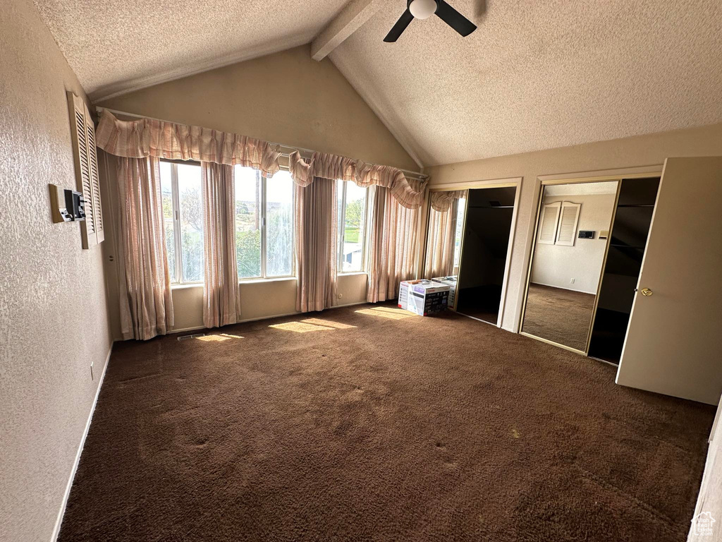 Unfurnished bedroom with ceiling fan, multiple closets, a textured ceiling, lofted ceiling with beams, and dark carpet