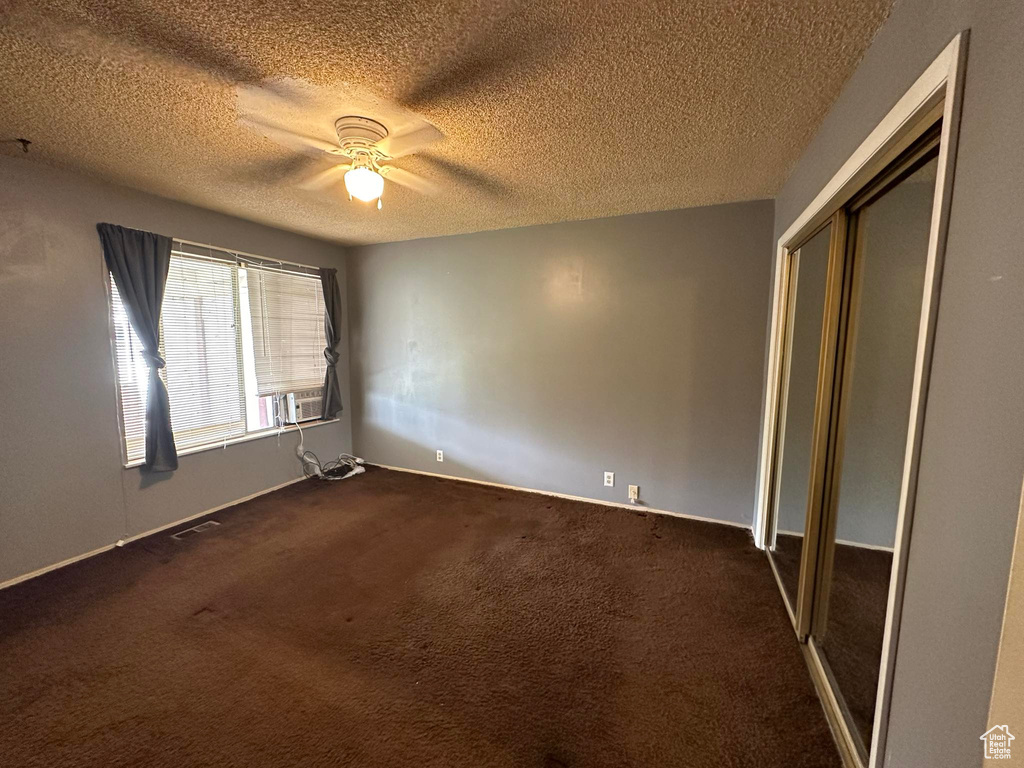 Unfurnished bedroom with dark colored carpet, a closet, ceiling fan, and a textured ceiling