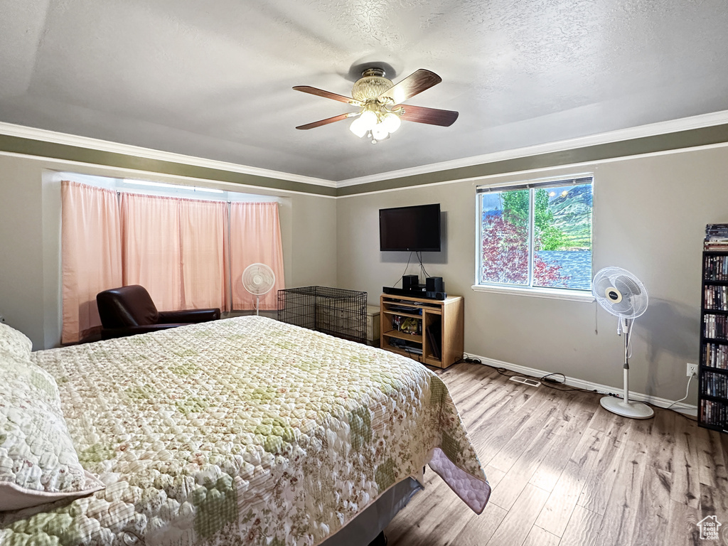 Bedroom featuring hardwood / wood-style floors, ceiling fan, ornamental molding, and a textured ceiling