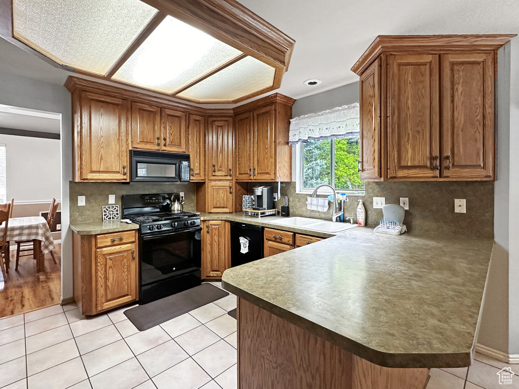 Kitchen featuring light hardwood / wood-style flooring, black appliances, backsplash, kitchen peninsula, and sink