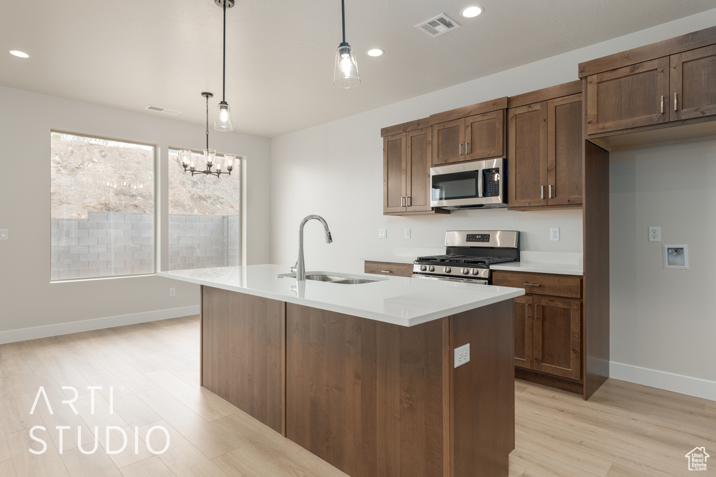 Kitchen with hanging light fixtures, light hardwood / wood-style flooring, an island with sink, stainless steel appliances, and sink