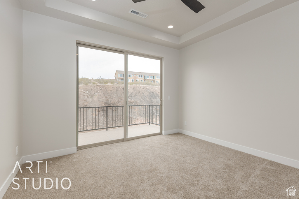 Carpeted empty room with ceiling fan and a raised ceiling