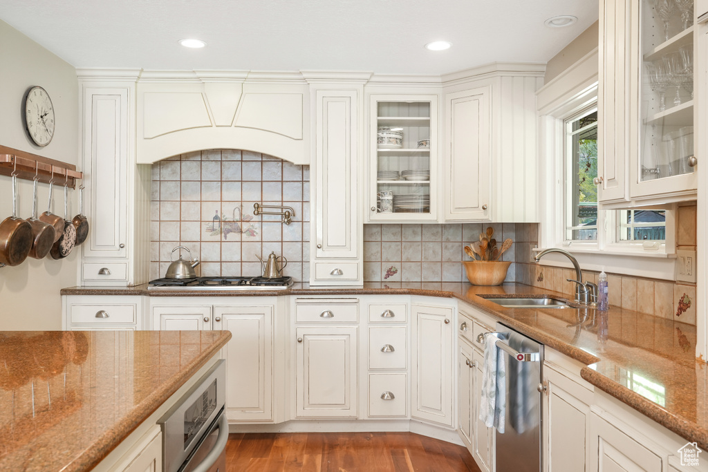 Kitchen with white cabinets, hardwood / wood-style floors, backsplash, appliances with stainless steel finishes, and sink