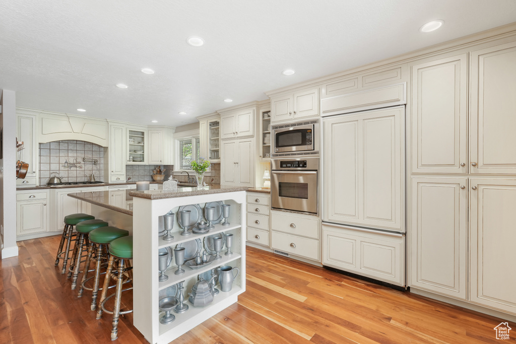 Kitchen featuring built in appliances, tasteful backsplash, a kitchen island, and light hardwood / wood-style floors