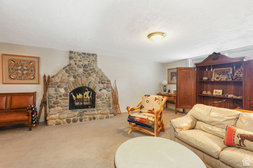 Carpeted living room featuring a stone fireplace and a textured ceiling