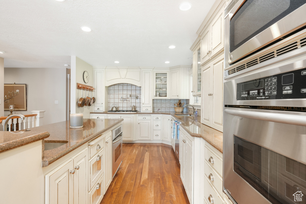 Kitchen featuring appliances with stainless steel finishes, sink, light hardwood / wood-style floors, backsplash, and light stone countertops