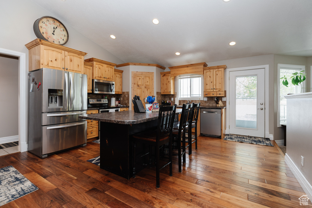 Kitchen with backsplash, stainless steel appliances, a center island, and hardwood / wood-style flooring