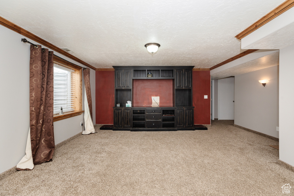 Unfurnished living room with ornamental molding, light carpet, and a textured ceiling