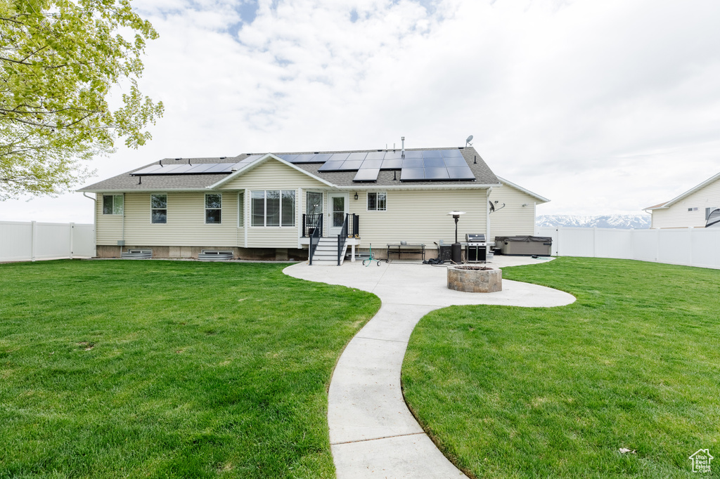 Rear view of property with solar panels, a yard, a fire pit, and a patio