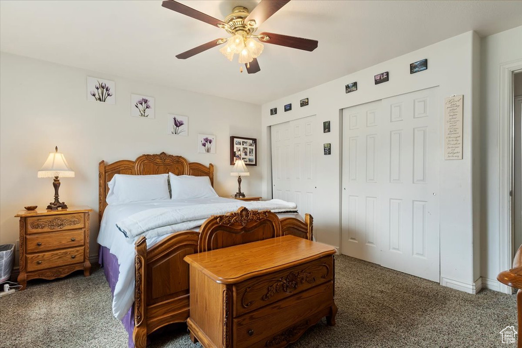 Bedroom with dark colored carpet, ceiling fan, and two closets