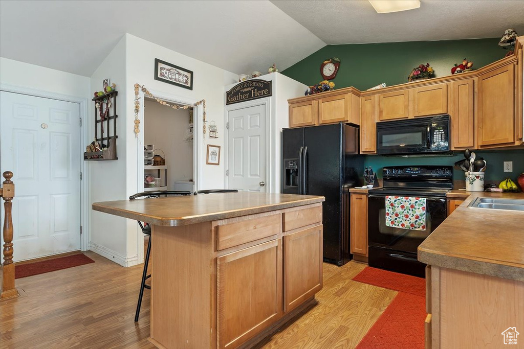 Kitchen featuring vaulted ceiling, light hardwood / wood-style flooring, a center island, and black appliances