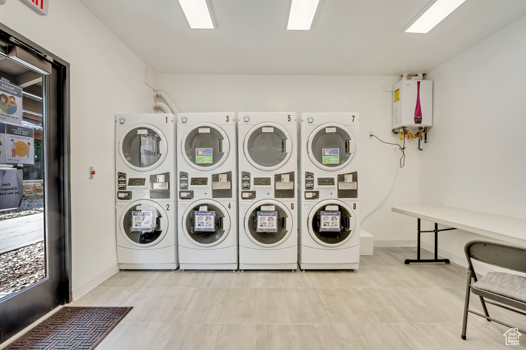 Clothes washing area with light tile flooring, tankless water heater, stacked washer / drying machine, and washing machine and clothes dryer
