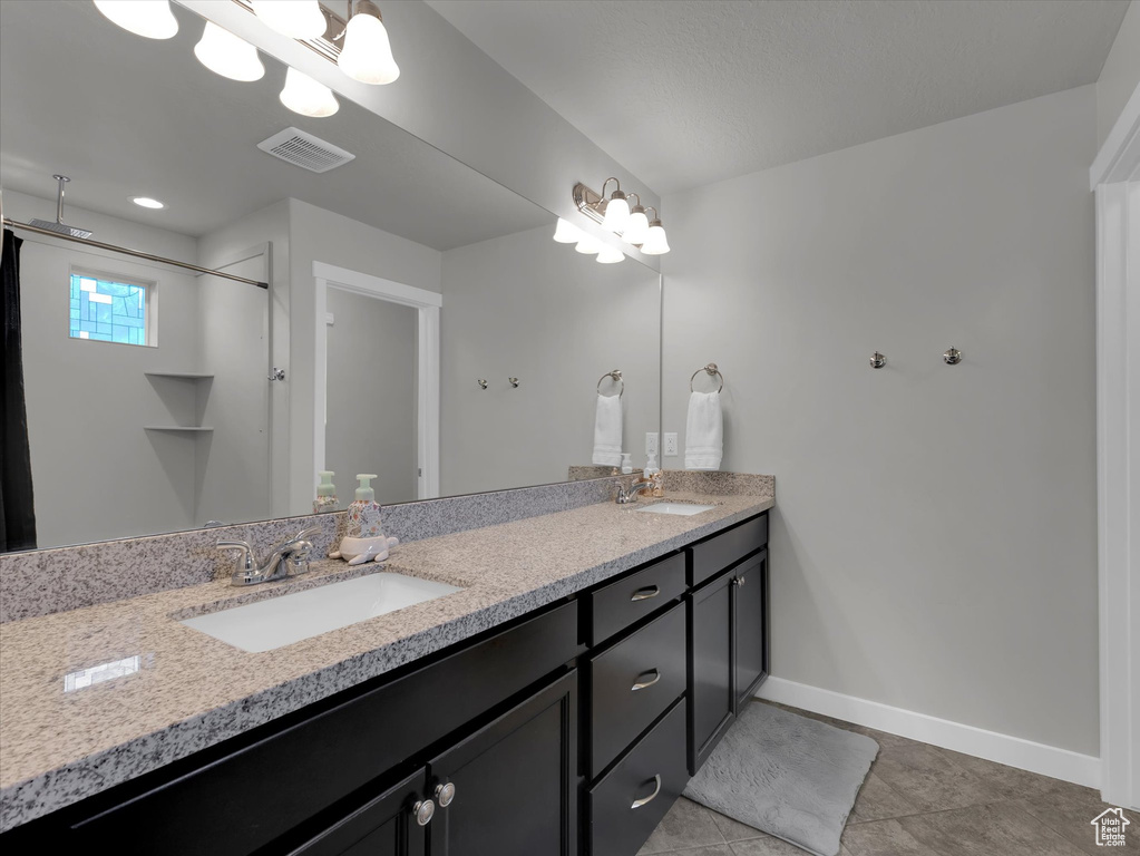 Bathroom featuring vanity with extensive cabinet space, dual sinks, and tile flooring