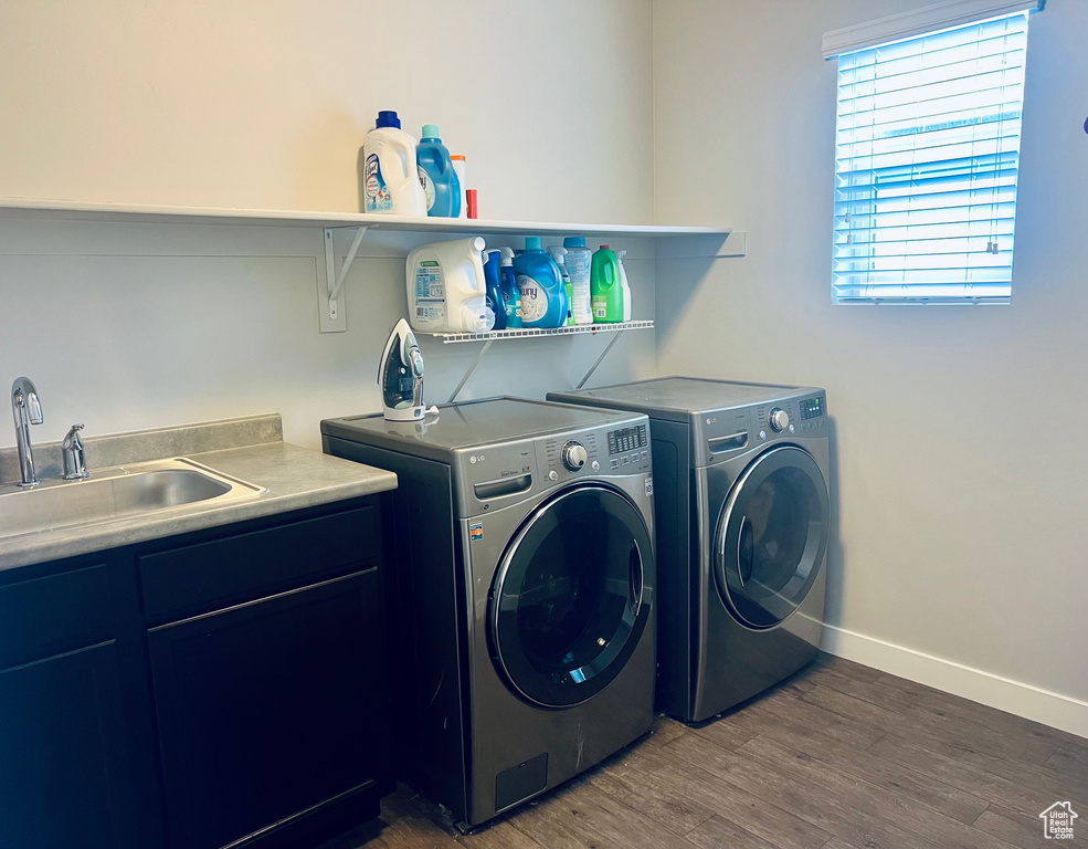 Washroom with sink, washing machine and dryer, hardwood / wood-style flooring, and cabinets